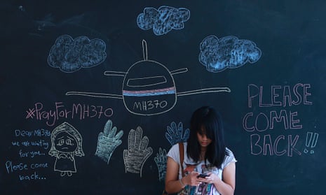 A woman uses her mobile phone as she stands against a chalkboard with messages for family members of passengers onboard the missing Malaysia Airlines Flight MH370, at an event to express solidarity in Subang Jaya March 16, 2014.
