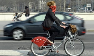 A woman rides a Velo'V, Lyon's bike share system, with a scarf covering her nose and mouth during an episode of heavy pollution in central Lyon