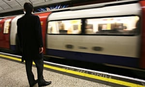 A man waits for a Northern Line underground train, tube, on a platform saying mind the gap