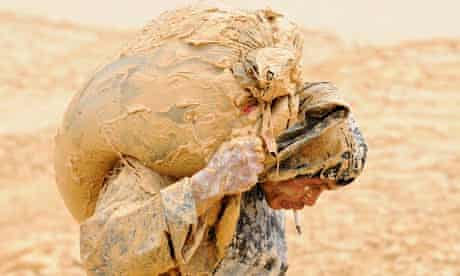 A man caked in wet mud struggles under a heavy load at a rare earth metals mine at Nancheng, China