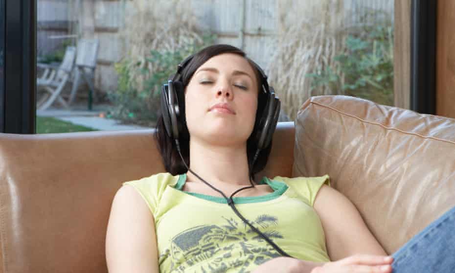 Woman listening to music on headphones on sofa.