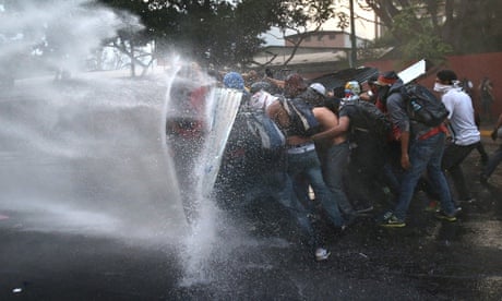 Venezuela protesters hold a barricade against a water canon fired by the National Guard