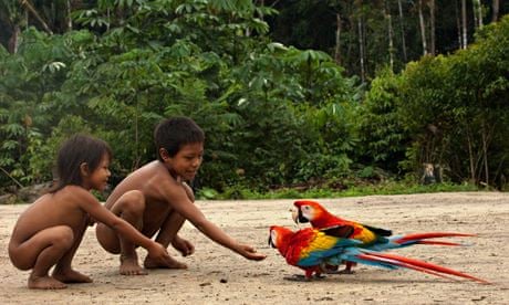 Huaorani Indian children play with scarlet macaws in Yasuni National Park