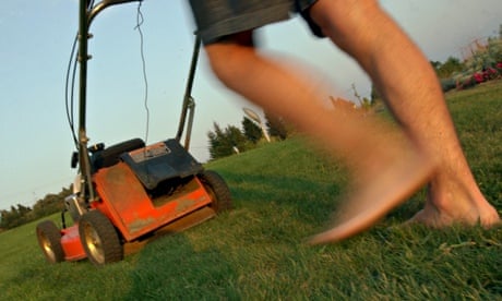 Legs of a barefoot man pushing an old lawn mower on long grass