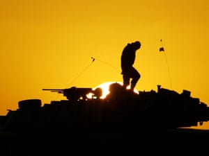 A US soldier walks on top of his armoured vehicle at sunset as he prepares for a night military exercise in the Kuwaiti desert south of the Iraq border in December 2002