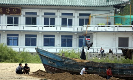 North Koreans sit by their boats on the bank of the Yalu River which separates the North Korean town of Sinuiju from the Chinese border town of Dandong, on 26 April, 2014.