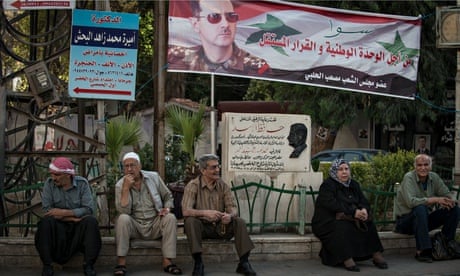Syrans in Damascus sit beneath a banner of Bashar al-Assad ahead of the presidential election