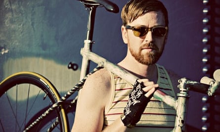 A fixed gear rider in a yellow striped tank top and sunglasses poses