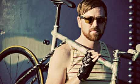 A fixed gear rider in a yellow striped tank top and sunglasses poses