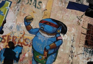 A boy prepares to fly a kite next to a graffiti by Brazilian artist Cranio depicting an indigenous man, in reference to the 2014 World Cup.