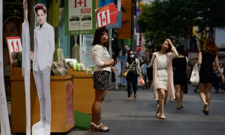 A shop assistant advertises a promotion outside a cosmetics shop next to cardboard cut-outs of popular entertainers, in central Seoul.