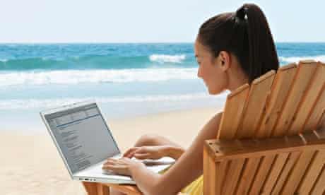 Mixed race woman using laptop on beach