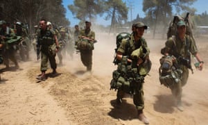 Israeli soldiers carry their gear as they walk towards a staging area outside the Gaza Strip.