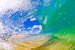 A surfer's perspective looking out of a crystal clear tube. The glassy & light wind conditions make the wave transparent and glass-like, showing the sand on the ocean floor, in Oahu, Hawaii.