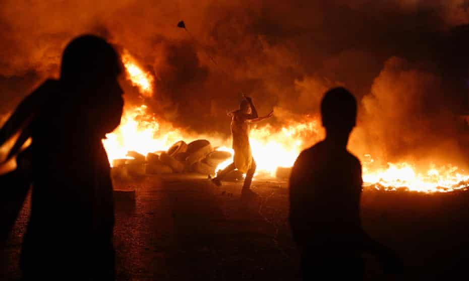 A Palestinian protester behind a barricade of burning tyres uses a slingshot to throw stones at Israeli troops near the West Bank city of Ramallah