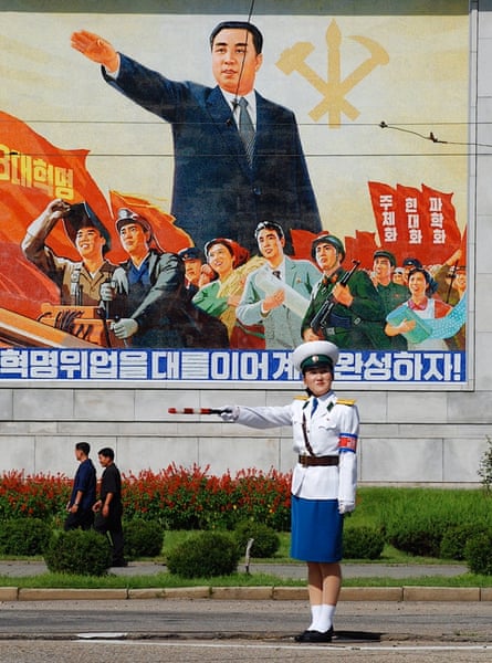 A policewoman directs traffic in front of a poster of North Korea's immortal president Kim Il-sung