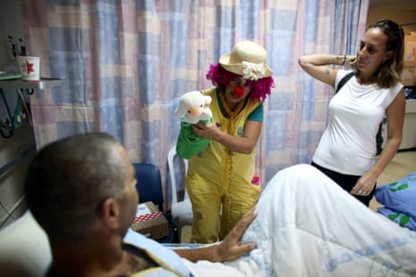 An Israeli woman dressed as a clown tries to cheer up an injured Israeli soldier who was wounded in fighting in the Gaza Strip, in the Soroka Hospital in Beersheba, Israel, 30 July 2014.
