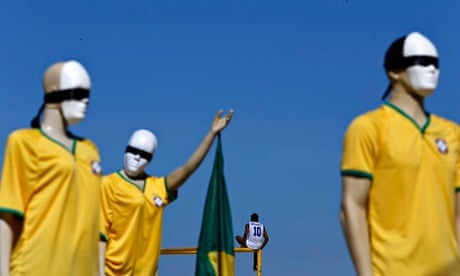 A man sits on top of a goal post next to mannequins that are part of a anti-Fifa demonstration,