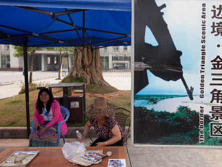 Two young women run a booth for tourists next to the Chinese border with Burma advertising tours to the 'Golden Triangle Scenic Area', in Daluo, the border town with Burma, Xishuangbanna, Yunnan Province, China.