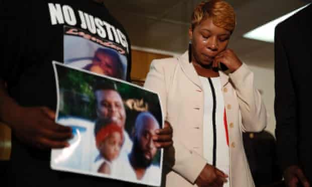 Lesley McSpadden, the mother of 18-year-old Michael Brown, wipes away tears as Brown's father, Michael Brown Sr, holds up a family picture of himself, his son, top left, and a young child.