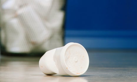 Discarded paper cup lying in front of full bin