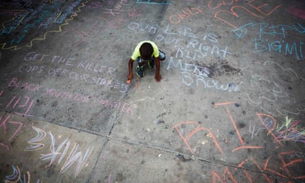 A boy adds a slogan on a pavement in Ferguson against the death of Michael Brown.