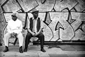 two men sitting on stools in front of a wall of graffiti