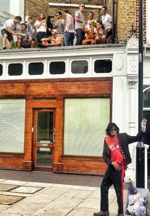 a man dressed as michael jackson standing by a lampost as young people watch from above