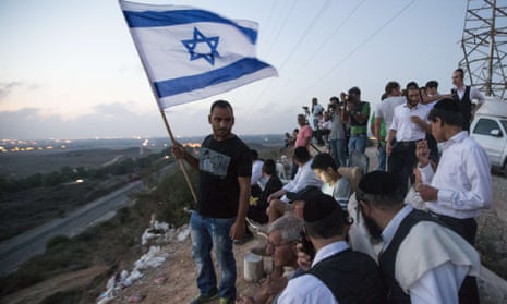 Israelis, mostly residents of the southern Israeli city of Sderot, stand with an Israeli flag on a hill overlooking the Gaza Strip, on July 20, to watch the fighting between the Israeli army and Palestinian militants.