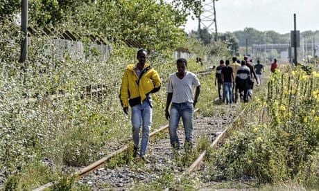 Migrants walk on a railway in Calais
