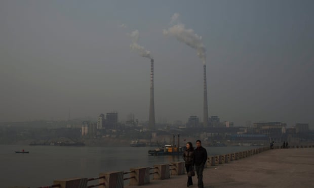 A couple walk on the riverside as two chimneys emit smoke at a power plant across the river in China's Chongqing municipality.