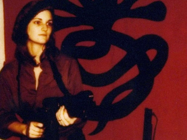 Patricia "Patty" Hearst, as "Tania" in front of a poster issued by the Symbionese Liberation Army.