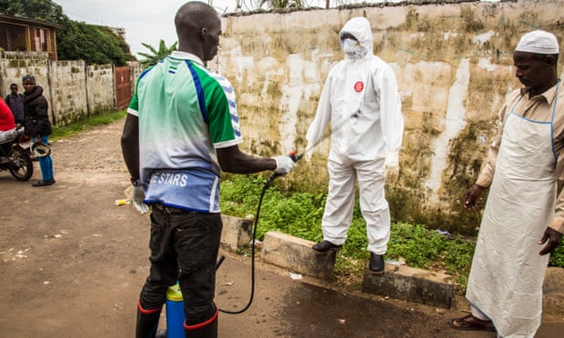 A health worker in a protective suit is sprayed with disinfectant by a colleague in Freetown, Sierra Leone