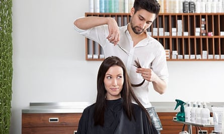 A woman having her hair cut in a salon by a man with a beard.