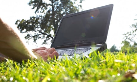 Typing on a pc laptop in a park on the grass under summer sun