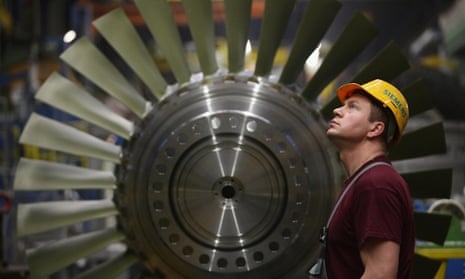 A worker watches as a turbine part moves above him while standing in front of a rotor assembly at the Siemens gas turbine factory in Berlin.