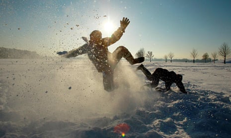 Two kids falling around and kicking up snow