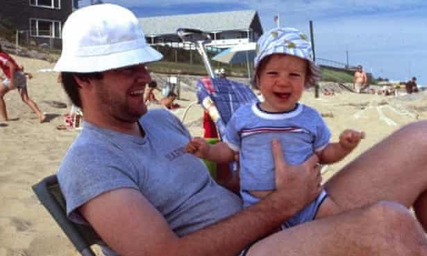 a man holding a baby boy whilst sitting on the beach