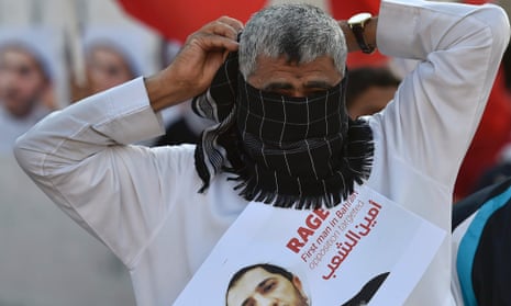 A protester covers his face while holding a picture of detained opposition leader Sheikh Ali Salman while facing-off Thursday with police in Bahrain