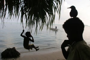 Children play on the beach, beside a fallen trunk of a coconut tree whose roots had been exposed by sea erosion of the land, on the shoreline of Han Island, Carterets Atoll, Papua New Guinea, on Monday, Dec. 11, 2006.  Rising sea levels have eroded much of the coastlines of the low lying Carteret islands (situated 80km from Bougainville island, in the South Pacific), and waves have crashed over the islands flooding and destroying what little crop gardens the islanders have. Food is in short supply, banana and swamp taro crops are failing due to the salt contamination of the land, and the islanders live on a meagre one meal per day diet of fish and coconut. There is talk by the Autonomous Region of Bougainville government to relocate the Carteret Islanders to Bougainville island, but this plan is stalled due to a lack of finances, resources, land and coordination.