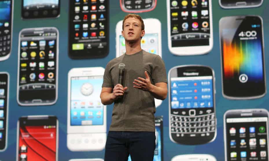 Mark Zuckerberg, microphone in hand, against a display of smartphones of all makes