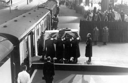 The coffin is loaded onto a train at Waterloo Station, with the Station Master standing to attention in the foreground