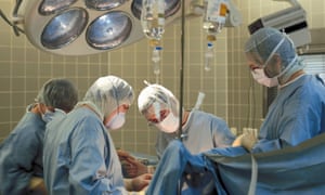 Four masked surgeons in gowns around a surgical bed; the patient is not visible.