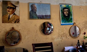 A Havana man is reflected in a mirror hanging on his wall covered with photographs of (L to R) Raul Castro, Fidel Castro, and fellow revolutionary Ernesto 'Che' Guevara.