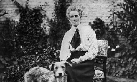 Black and white photo; Cavell is sat on a dining chair outside, a garden wall behind her. Her hair is tied back, slightly bouffant, and she is wearing a striped pale blouse, long dark skirt, and wide dark tie or cravat. She is petting a large dog.