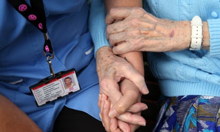 A carer holds the hand of an elderly lady