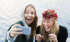 Two young women laughing and filming themselves with a mobile phone.