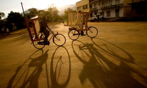 Two cyclists carrying furniture make their way through the streets of Kasese in western Uganda