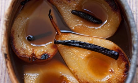 Four baked pear halves, with vanilla pods on top, sitting in syrup