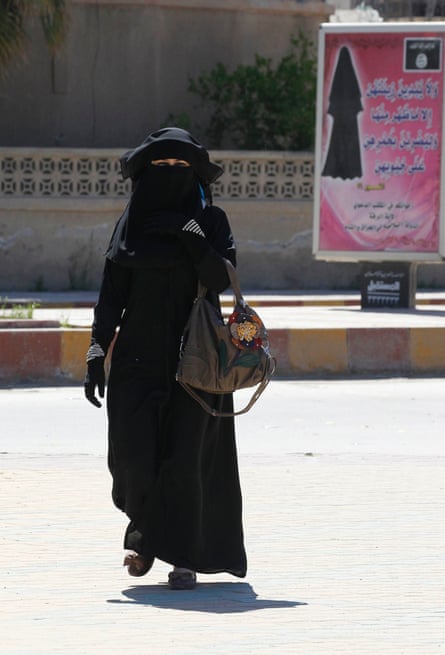 A veiled woman walks past a billboard urging women to wear a hijab